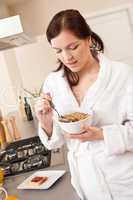 Happy woman eating cereals for breakfast in kitchen