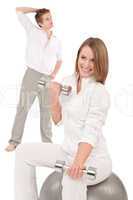 Young couple with weights and fitness ball on white