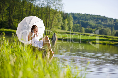 Happy romantic woman sitting by lake with parasol