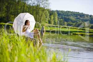 Happy romantic woman sitting by lake with parasol