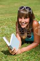 Smiling young woman lying down on grass with book