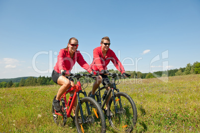 Young couple riding mountain bike in spring meadow