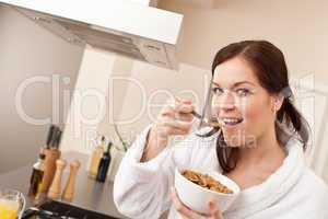 Happy woman eating cereals for breakfast in kitchen