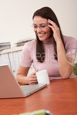 Smiling secretary with coffee and laptop at office