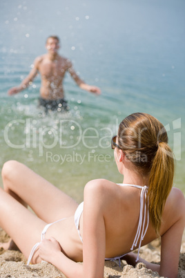 Couple on beach - woman in bikini sunbathing
