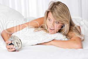 White lounge - Young woman surprised holding alarm clock