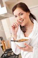 Happy woman eating cereals for breakfast in kitchen