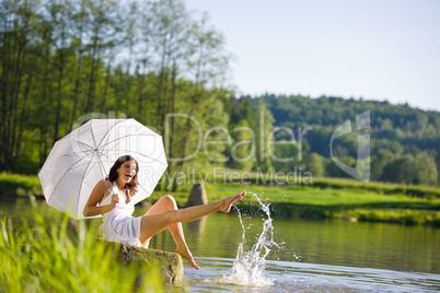 Happy romantic woman sitting by lake splashing water