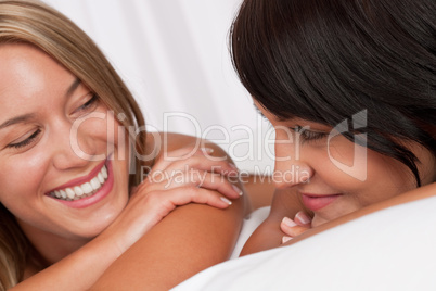 Portrait of two smiling women lying down in white bed