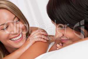 Portrait of two smiling women lying down in white bed