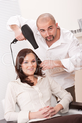 Professional hairdresser with hair dryer at salon with customer