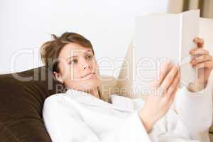 Young woman read book on sofa wearing bathrobe