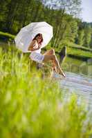 Happy romantic woman sitting by lake holding parasol