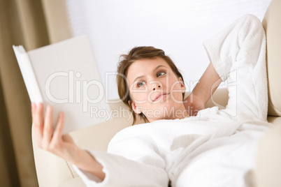 Young woman read book on sofa wearing bathrobe