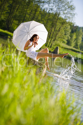 Happy romantic woman sitting by lake splashing water