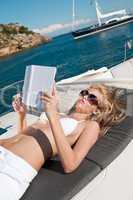 Blond woman lying on yacht reading book