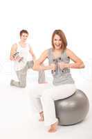 Young couple with weights and fitness ball on white