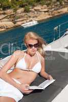 Blond woman lying on yacht reading book
