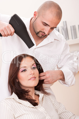 Professional hairdresser with hair dryer at salon with customer