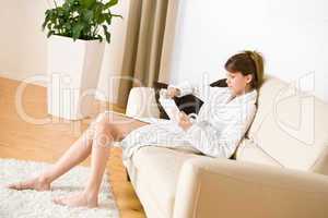 Young woman read book on sofa wearing bathrobe