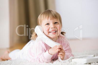 Smiling little girl lying down on carpet with phone