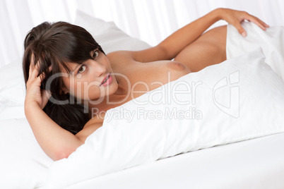 Naked woman looking at camera in white bed