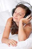 Happy woman lying on white sofa listening to music