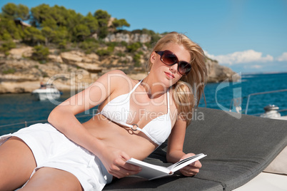 Blond woman lying on yacht reading book