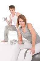 Young couple with weights and fitness ball on white