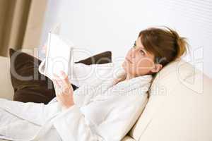 Young woman read book on sofa wearing bathrobe