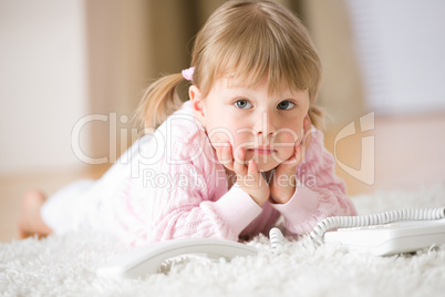 Little girl with telephone lying down on carpet