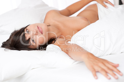 Smiling woman lying naked in white bed