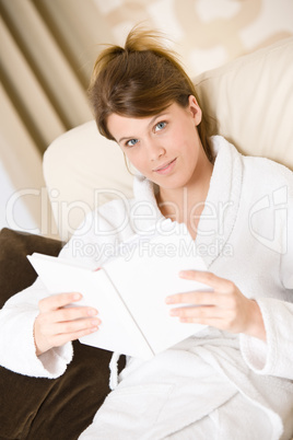 Young woman read book on sofa wearing bathrobe