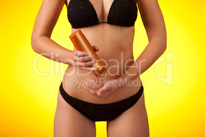 Part of female body wearing black bikini  and bottle of suntan c