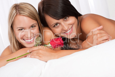 Portrait of two smiling women lying down in white bed