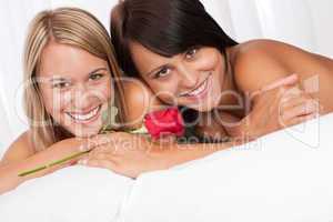 Portrait of two smiling women lying down in white bed