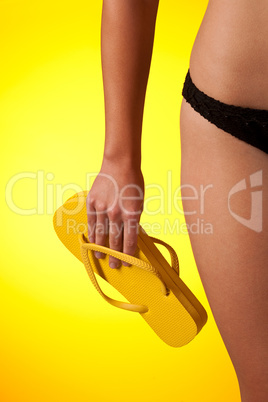 Part of female body wearing black bikini  and holding flip-flop