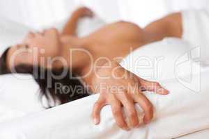 Naked woman lying in bed, focus on hand