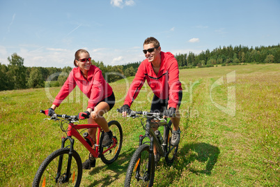 Young couple riding mountain bike in spring meadow