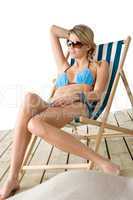 Beach - Young woman in bikini sitting on deck chair