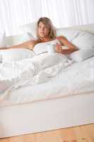 White lounge - Blond woman lying in white bed drinking coffee