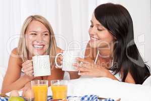 Two women having home made breakfast in white bed