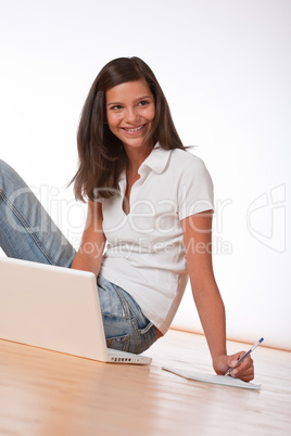 Smiling teenager sitting with laptop and writing notes