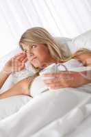 White lounge - Blond woman lying in white bed holding cup of cof