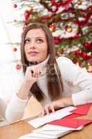 Young woman thinking while writing Christmas card