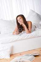 Young woman lying on bed writing notes