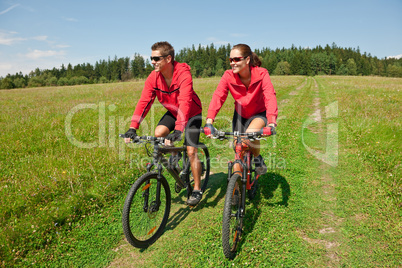 Young couple riding mountain bike in spring meadow