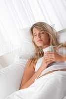 White lounge - Young woman relaxing on bed holding cup of coffee