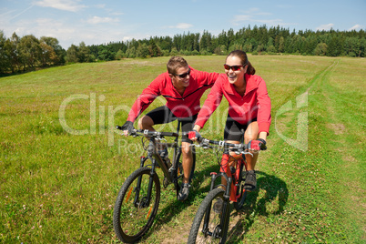 Young couple riding mountain bike in spring meadow