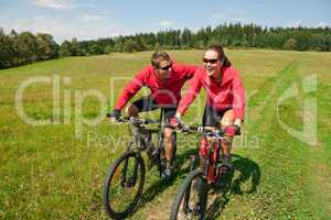 Young couple riding mountain bike in spring meadow
